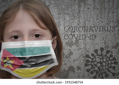 Little Girl In Medical Mask With Flag Of Mozambique Stands Near The Old Vintage Wall With Text Coronavirus, Covid, And Virus Picture. Stop Virus