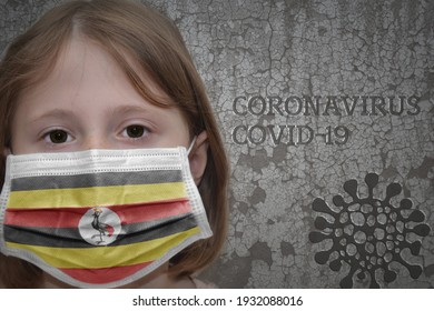 Little Girl In Medical Mask With Flag Of Uganda Stands Near The Old Vintage Wall With Text Coronavirus, Covid, And Virus Picture. Stop Virus