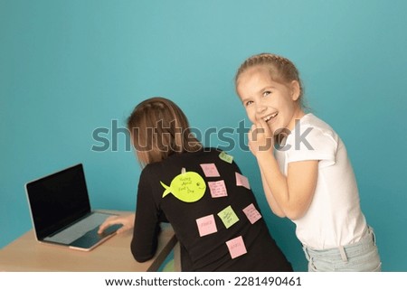 Little girl with mom and joke sticker on back against blue background April fool's day. date 1 April.