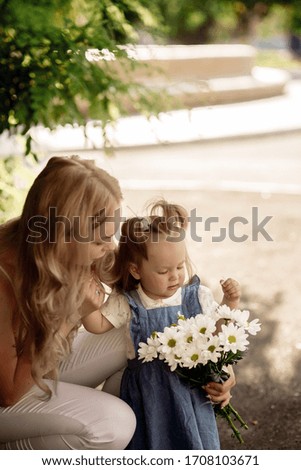 Little girl with mom sniff a bouquet of daisies
