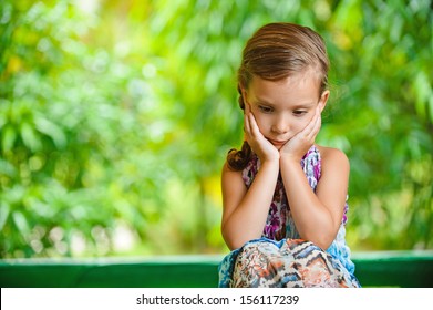 Little girl on a green lawn leans against chair and thinks of mother.