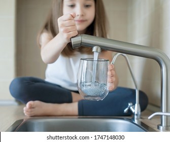 Little Girl Open A Water Tap With Her Hand Holding A Transparent Glass. Kitchen Faucet. Filling Cup Beverage. Pouring Fresh Drink. Hydration. Healthcare. Healthy Lifestyle. World Water Day