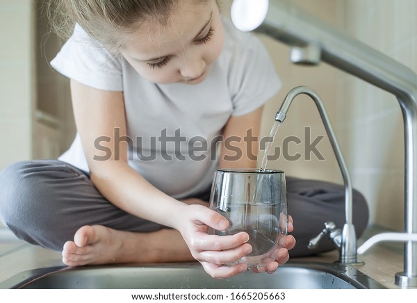 Little girl open a water tap with her hand holding a\
transparent glass. Kitchen faucet. Filling cup beverage. Pouring\
fresh drink. Hydration. Healthcare. Healthy lifestyle. World Water\
Day