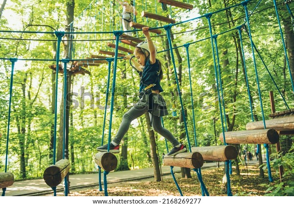 Little girl overcomes the obstacle in the rope park.\
Child enjoying activity in a climbing adventure park on a summer\
day. 