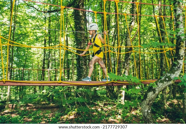 Little girl overcomes the obstacle in the rope park.\
Child enjoying activity in a climbing adventure park on a summer\
day. 