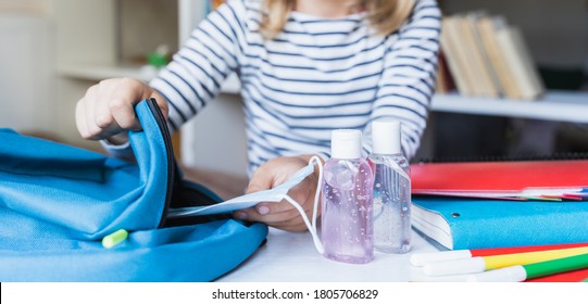 Little girl packing blue backpack in kids's room. Face mask, bottle of sanitizer, stationery, pens, multicolored markers, notebooks. Back to school. Mom's hygiene,safety precautions after coronavirus. - Shutterstock ID 1805706829