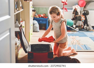 Little girl packing suitcase at home. Cute child putting clothes into suitcase. Preparing for family vacations with children. Practicing independence