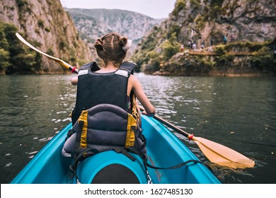 Little Girl Paddles A Canoe With Full Equipment In A Scenic River Canyon. Shot From The Back, No Face. Children In Sport.  Kayak For Kids.