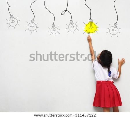 little girl with paintbrush creative drawing light bulb ideas on wall, back view
