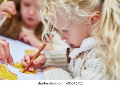 Little Girl Painting Autumn Leaves In Arts & Crafts Class