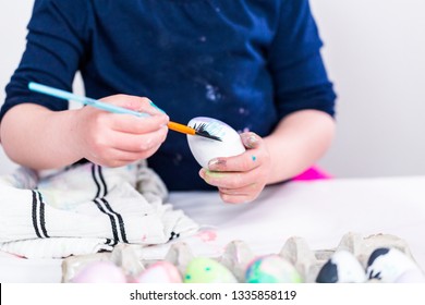 Little girl painting craft Easter eggs with acrilic paint.