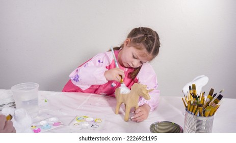 Little girl painting paper mache figurine at homeschooling art class.