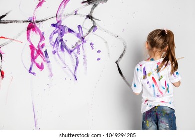 Little girl painting a white wall with colorful paint. Messy fun. Child's creativity development.