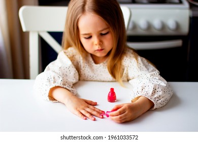 Little girl paints her nails with pink nail polish. Cute toddler girl  playing with colorful nail polish doing manicure. Cosmetics and beauty concept.
