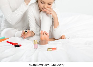 Little girl in pajamas applying nail polish to toenails on bed