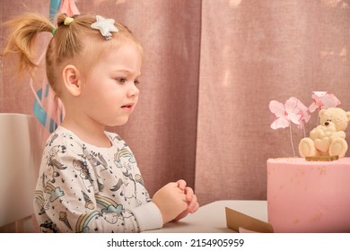 A little girl in pajamas on her birthday sits on a white chair at a children's table, on which there is a birth