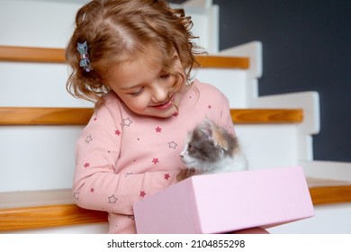 a little girl in pajamas is sitting at home on the stairs playing with a kitten