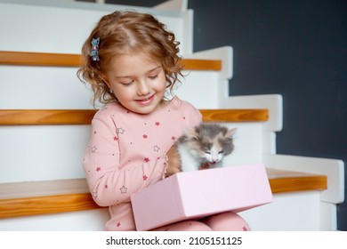 a little girl in pajamas is sitting at home on the stairs playing with a kitten