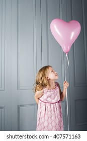 little girl in party dress looking at her pink heart shaped balloon