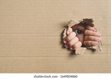 Little Girl Peeking From A Hole On Cardboard Box. Concept Of A Human Trafficking, Spying And Curiosity