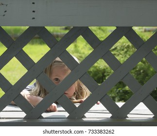 Little Girl Peeking Through A Lattice Deck Rail