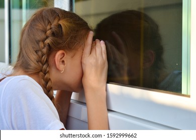 A Little Girl Peeps Through Someone Else's Window. Child Girl Looking Out The Window. A Teenager Girl Spying Inside The House. Spy On Other People. Look Through The Window.