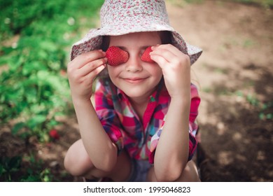 Little girl picking strawberry on a farm field.  Strawberry in a kid hand against background of flowers. - Powered by Shutterstock