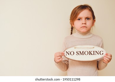 A little girl with pigtails on a beige background holds a sign with the words no smoking in her hands. No smoking day.  Children Protection Day. The child is against smoking, for a halthy lifestyle. 