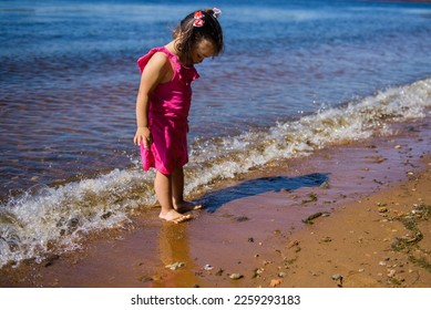 A little  girl in a pink dress by the water. The child walks in nature. - Powered by Shutterstock