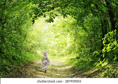 A little girl in a pink dress fun runs on the road in the fairy forest