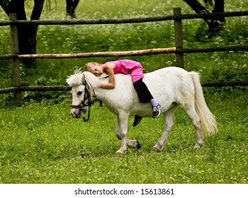 Little girl in pink dress riding white pony on green grass field