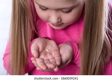 Kleines Mädchen auf Rosa hält einen gefallenen Milchzahn in ihren Handflächen