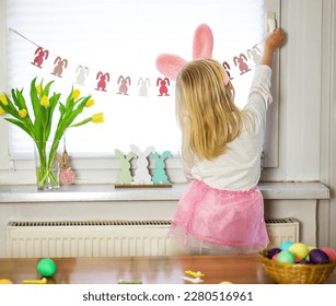 Little girl in pink rock and white shirt decorating room for Easter. Preparation for happy Easter. - Shutterstock ID 2280516961