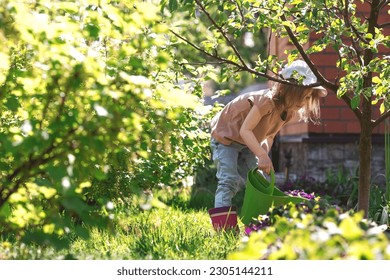 A little girl in pink rubber boots is watering flowers from a watering can in a summer garden, outdoors. The concept of gardening and teaching a child to work. - Powered by Shutterstock