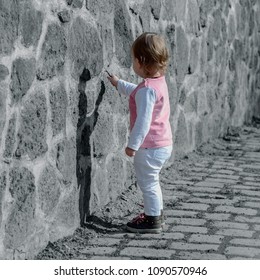 little girl in pink white clothes writes a wooden stick on a stone wall