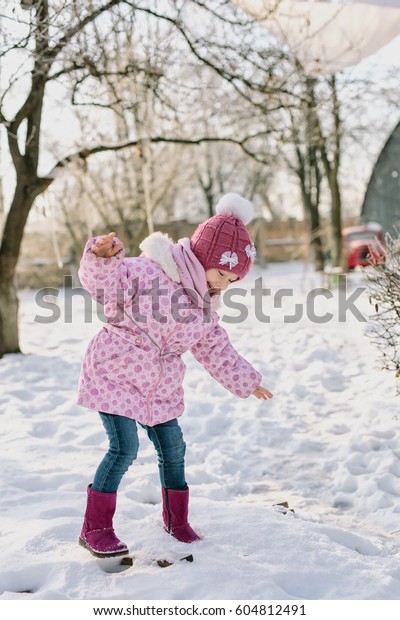 A little girl in a pink winter\
jacket and hat is having fun on the snow on a winter sunny\
day