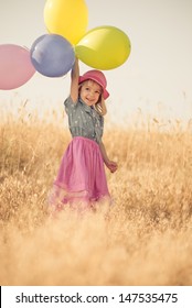 Little girl playing with balloons on wheat field