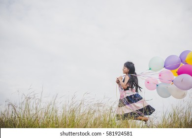 Little girl playing with balloons on meadows field.