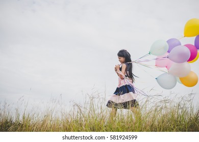 Little girl playing with balloons on meadows field.