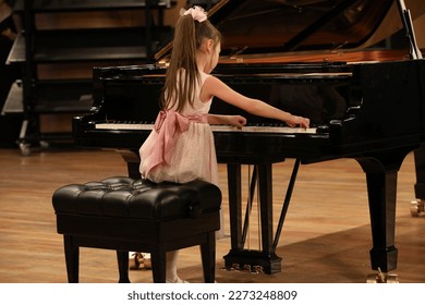 A little girl playing a big black piano - Powered by Shutterstock