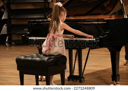 A little girl playing a big black piano