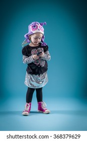 Little Girl Playing With Cellphone In Cute Outfit With High Top Tennis Shoes - Looking Down At Cellphone.