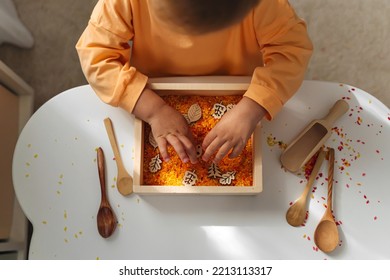 A little girl playing with colored rice in autumn sensory bin. Montessori material. Scooping and pouring activity for kids. Games for learning and development of the child. - Shutterstock ID 2213113317