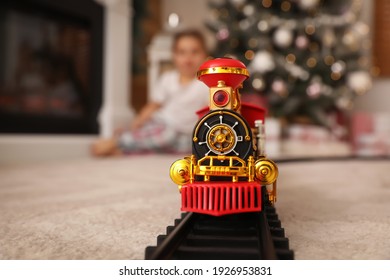 Little girl playing with colorful toy in room decorated for Christmas, focus on train
