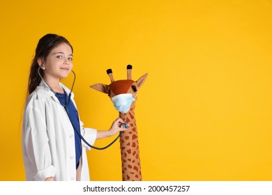 Little girl playing doctor with toy giraffe on yellow background, space for text. Pediatrician practice