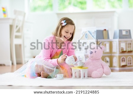 Little girl playing with doll house in white sunny bedroom. Kid with toys. Role game for young children. Child with teddy bear toy. Kids play tea party with stuffed animals and dolls. Nursery interior