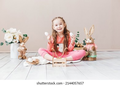 Little Girl Playing With Easter Toy Bunnies And A Basket Of Easter Eggs. Child Celebrating Easter. Easter Egg Hunt. Home Decoration, Bunnies And Flowers