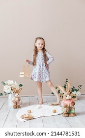 Little Girl Playing With Easter Toy Bunnies And A Basket Of Easter Eggs. Child Celebrating Easter. Easter Egg Hunt. Home Decoration, Bunnies And Flowers