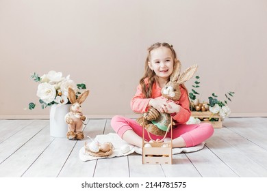 Little Girl Playing With Easter Toy Bunnies And A Basket Of Easter Eggs. Child Celebrating Easter. Easter Egg Hunt. Home Decoration, Bunnies And Flowers