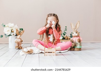 Little Girl Playing With Easter Toy Bunnies And A Basket Of Easter Eggs. Child Celebrating Easter. Easter Egg Hunt. Home Decoration, Bunnies And Flowers